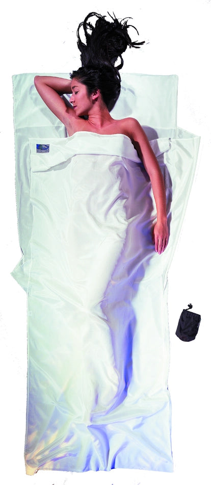 Housse de lit de voyage adulte en coton et soie Cocoon - Blanc - mise en situation : une personne dort dans le drap, la pochette placée juste à côté.