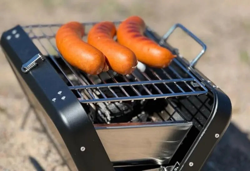 Barbecue à charbon pliable portatif de kikirikit noir - gros plan sur la grille de cuisson avec  saucisses qui cuisent