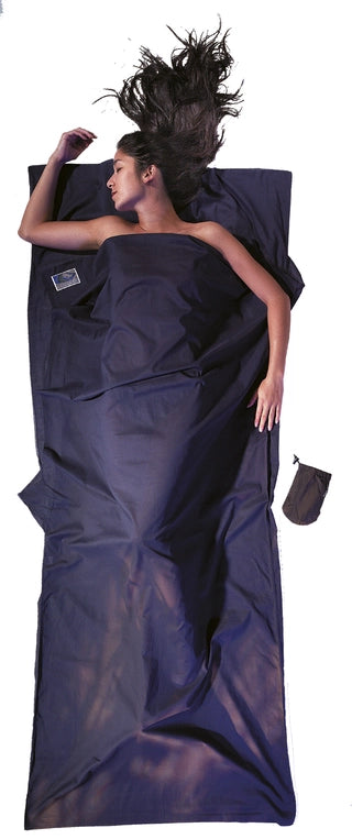 Housse de lit de voyage adulte en coton Egyptien de Cocoon - Marine - Housse de lit adulte en coton et soie Cocoon – bleu – mise en situation : une personne dort dans le drap, la pochette placée juste à côté.