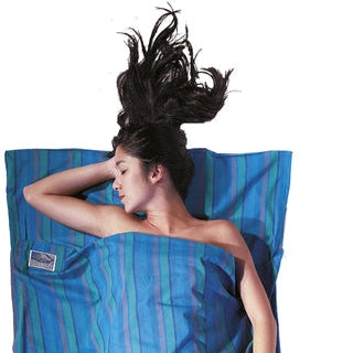 Housse de lit de voyage zippée en coton de Cocoon - bleu - Mise en situation : une personne dort dans la housse de lit avec la pochette posée à côté, utilisée en version simple
