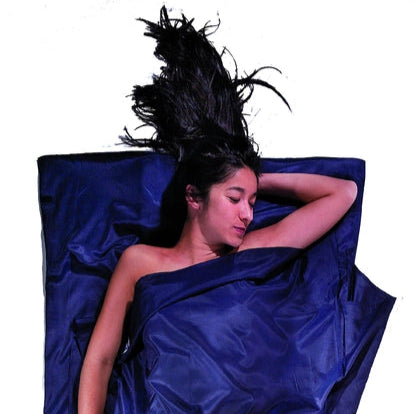Housse de lit de voyage adulte en coton et soie Cocoon - Marine - mise en situation : une personne dort dans le drap, la pochette placée juste à côté.