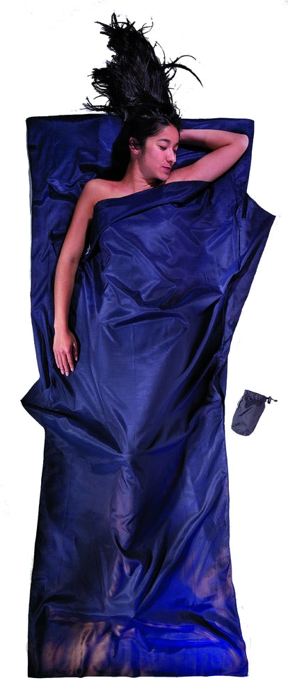 Housse de lit de voyage adulte en coton et soie Cocoon - Marine - mise en situation : une personne dort dans le drap, la pochette placée juste à côté.