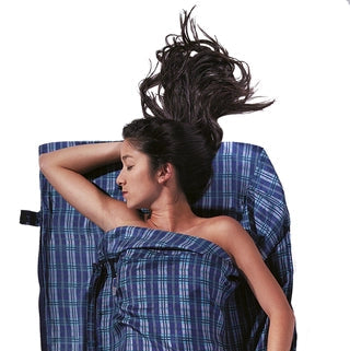 Housse de lit de voyage  zippée en soie de Cocoon - carreaux bleu en soie - Mise en situation : une personne dort dans la housse de lit avec la pochette posée à côté, utilisée en version simple