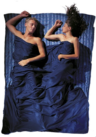 Housse de lit de voyage zippée en soie de Cocoon – motif à carreaux bleus en soie – mise en situation : deux personnes dorment dans la housse, utilisée en version double