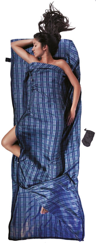 Housse de lit de voyage zippée en soie de Cocoon - carreaux bleu en soie - Mise en situation : une personne dort dans la housse de lit avec la pochette posée à côté, utilisée en version simple