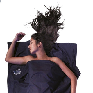 Housse de lit de voyage adulte en coton Egyptien de Cocoon - Marine - Housse de lit adulte en coton et soie : une personne dort dans le drap, la pochette placée juste à côté.