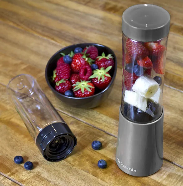 Mini Blender Detoximix gris – Mise en situation avec des fruits entiers dans la bouteille de 280 ml et une bouteille supplémentaire présentée couchée.