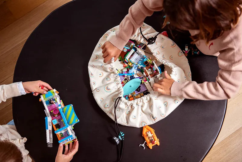 Mini sac de rangement et tapis de jeux motif arc-en-ciel de Playandgo - vue du sac ouvert avec des jeux sur une table et des enfants qui jouent