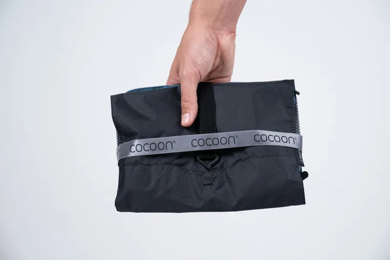 Trousse de toilette accrochable Cocoon – bleu – vue de face de la trousse pliée avec un ruban Cocoon, portée à la main.