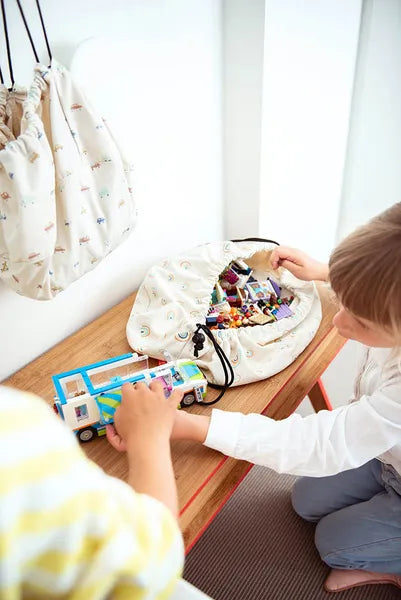 Mini sac de rangement et tapis de jeux motif arc-en-ciel de Playandgo - vue du sac ouvert sur un banc avec des jeux et un enfant qui joue avec les jeux